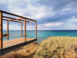 A timber-framed observation deck over the turquoise waters of the Mediterranean against a dramatic sky.