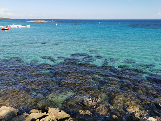 Obraz premium View of the clear water of the Mediterranean Sea, the pier on the Fig Tree Bay beach with a boat and catamarans and the island.