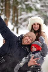 Family of mother, father and son having fun in snowy winter wood with cheerfull pet dog.