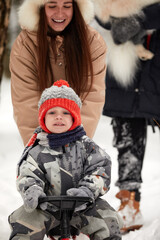 Family of mother, father and son having fun in snowy winter wood with cheerfull pet dog.