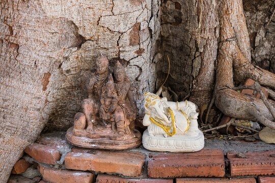 old clay broken statue of the hindu god are laid under a tree in a Thai temple.