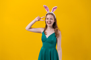 Shot happy girl in fluffy pink bunny ears, points fingers to side, demonstrates something over an empty space isolated on a yellow studio background. Easter holiday concept