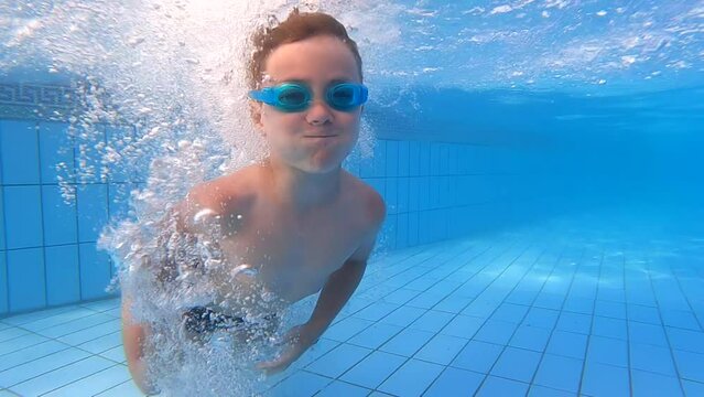 A little boy swims underwater in a protective mask in the pool on a sunny day, slow motion