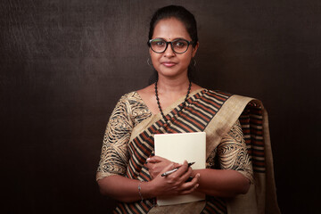 Portrait of a happy woman of Indian ethnicity wearing sari and holding a book in hand