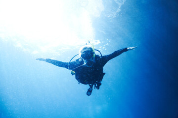 Soaring in the ocean depths. A scuba diver descending towards you with her arms wide open -...
