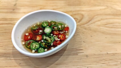 Fish sauce with chilli in white bowl on wooden table. Traditional Thai fish sauce style with red and green chilli.