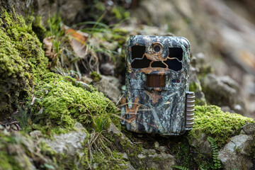 Camouflaged trail camera standing on a moss covered rocks in nature. Wildlife monitoring device...