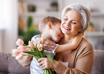Cheerful little boy giving flowers to grandmother