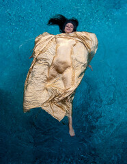 woman floats lying on her back in the turquoise water of the pool covered by a golden cloth under...