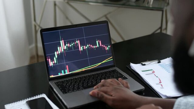 Stock exchange, trading online, cryptocurrency concept. African american trade broker works on stock market, analyze the graph of growth or fall of cryptocurrency on laptop, predicts the stock market