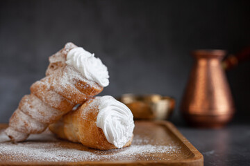 Puff pastry horns filled with white cream and falling powdered sugar