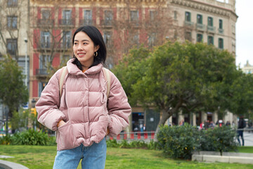 Fototapeta na wymiar Asian pretty girl with a backpack smiles in a city park on a cold day.