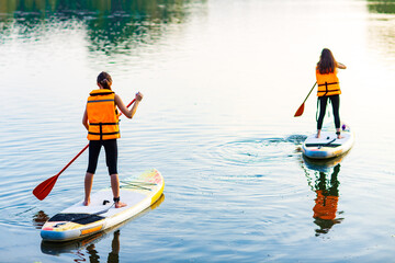 two young women in orange life jacket on supboard at river