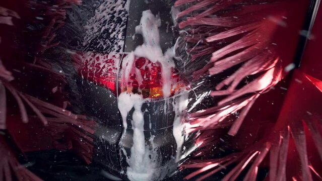 Black car moving though automatic car wash machine. The brush moving to clean tailgate and light. Slow motion shot