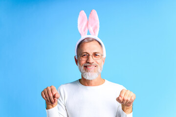 Cute mature man with bunny ears ready to Easter festivale on blue color background