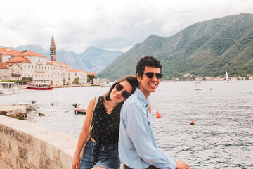 Fototapeta na wymiar Young couple travelers sitting and smiling at the seaside in Kotor Bay