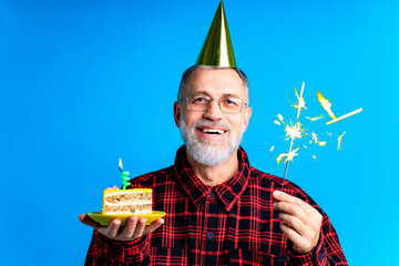 man wearing birthday hat with cake isolated on bright blue colour background, studio portrait