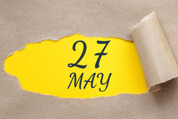 may 27. 27th day of the month, calendar date. Hole in paper with edges torn off. Yellow background is visible through ragged hole.Spring month, day of the year concept
