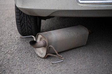 Car exhaust, muffler fallen down on the ground in traffic road, left behind the car in background....