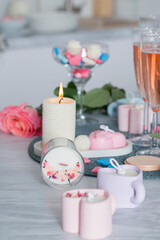 A candle in a glass with a singing wick decorated with dried flowers on the background of other candles, a peony rose and champagne.