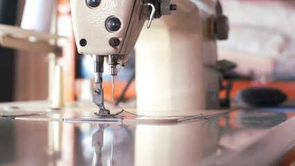 Industrial sewing machine needle steel presser foot with thread for sew cloth vintage tone close-up.