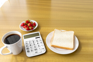 電卓と朝食（食パン、苺、コーヒー）。食費のイメージ