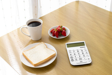 電卓と朝食（食パン、苺、コーヒー）。食費のイメージ