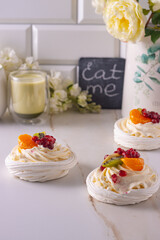Obraz na płótnie Canvas dessert pavlova with cream and fruits on gray plate white scandic ground white spring flowers matcha tea