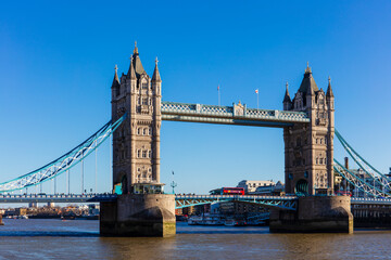 Tower Bridge with a red bus crossing on a sunny day with blue sky