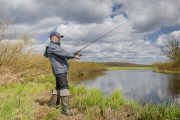 Fisherman throws spinning rod on the river bank.