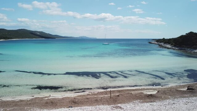 Sandy beach with the crystal blue Mediterranean sea and a sailing boat in the summer, 4K drone footage in Dugi otok, Croatia