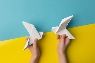 Children's hands hold two white birds as a symbol of peace on blue and yellow pastel paper color. No war. Stop war