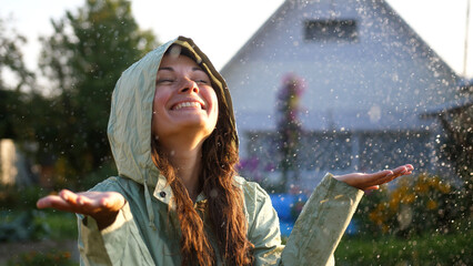 Young happy woman wearing green raincoat is feeling free and smiling under the rain. Concept of life, freedom, nature, adventure, purity.