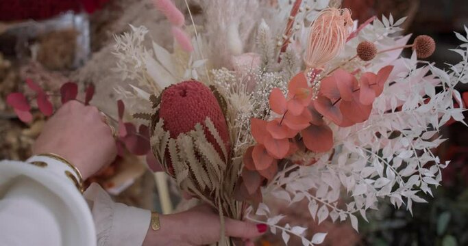 Hands of woman with golden rings and bracelet add last touches to majestic flower bouquet