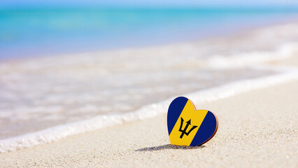 Flag of the Barbados in the shape of a heart on a sandy beach. The concept of the best vacation in...