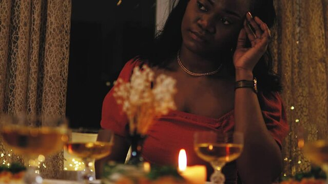Lonely sad depressed upset young african black female adult sitting at table with dinner, lonely celebration birthday. Lonely party alone during coronavirus, lockdown. Cozy evening with candles