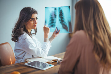 Fototapeta premium Professional female doctor and radiologist giving a consultation to his patient, he is examining and x-ray image and pointing. 