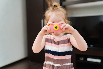 a funny little girl takes a photo on a little pink toy camera. 