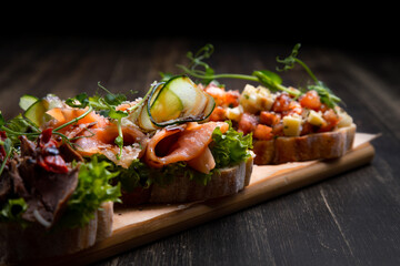 a dish of 3 different tapas stuffed with meat, fish and various microgreens, served on a board against a dark background - obrazy, fototapety, plakaty