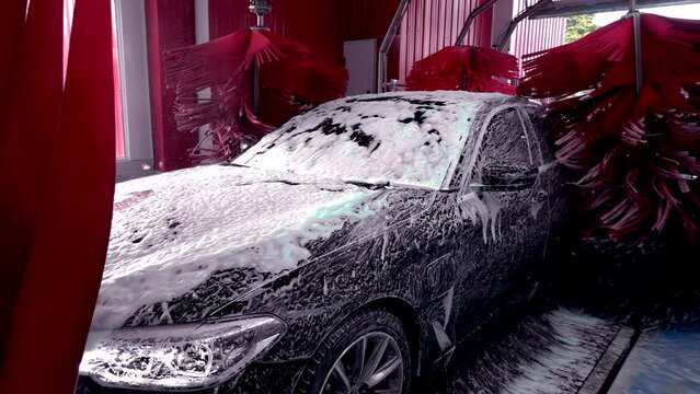 Black car moving though automatic car wash machine.Brush moving to clean the car. Slow motion shot