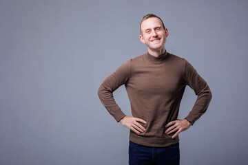 Male emotional portrait isolated on gray background. A man is dressed in a brown warm sweater, he has a smile on his face