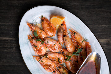 shrimps with lemon and sauce on a white plate on a dark background