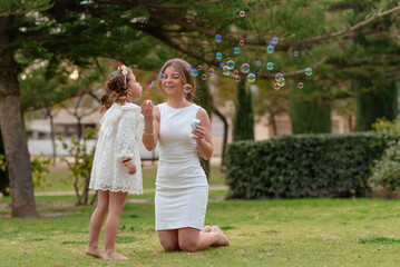 Mother and daughter blow soap bubbles outdoors.