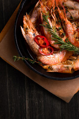spicy langoustines with pepper and rosemary in a frying pan, served with a glass of wine