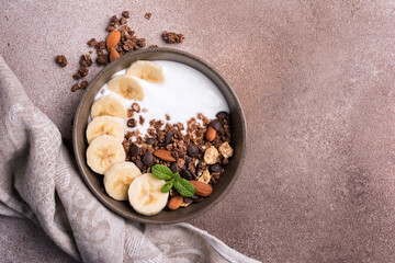 Healthy breakfast of granola with fresh banana, nuts, chocolate drops and yogurt