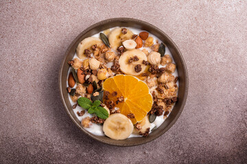 Healthy breakfast of granola with nuts, banana, orange and yogurt