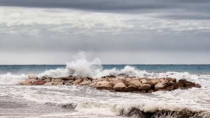 Sea waves crashing strongly against a breakwater near the shore of the beach on a day of rough seas and bad weather