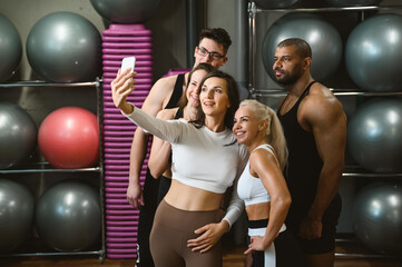 Group of multi racial sports people in the gym taking a selfie - Happy sports friends in the weight room while exercising - Lifestyle and sports concepts in a fitness club