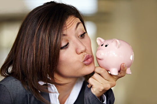 Cash is a girls best friend. An attractive businesswoman pulling a kissing face at her piggybank.