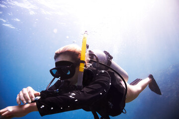 Time to descend. Young female scuba diver floating through the water as she checks her dive...